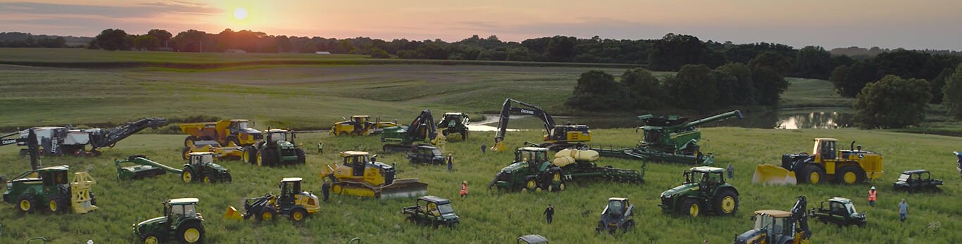 Människor som går bland flera typer av utrustning från John Deere på ett stort fält.