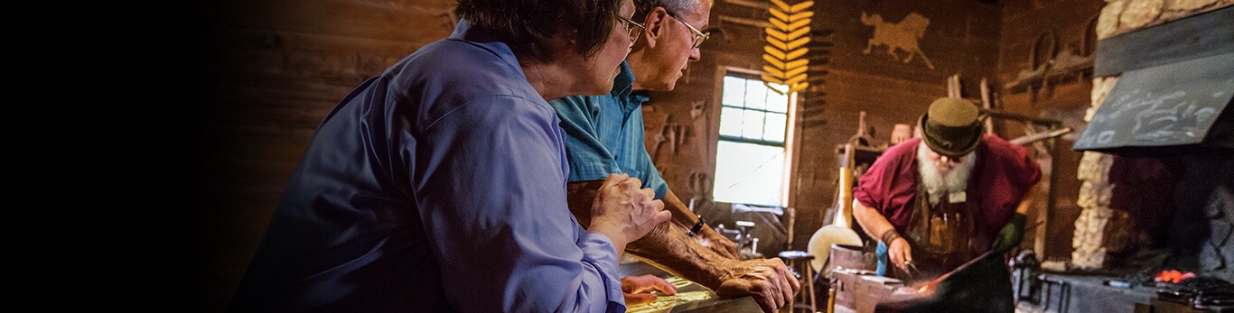 Äldre par ser på när en smed arbetar med en del av en metallhammare på en historisk plats i Grand Detour, Illinois, USA.
