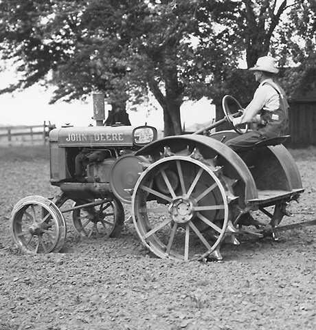 Historisk John Deere "GP" General Purpose-traktor som drar en jordfräs av modell John Deere nr 7 på fält