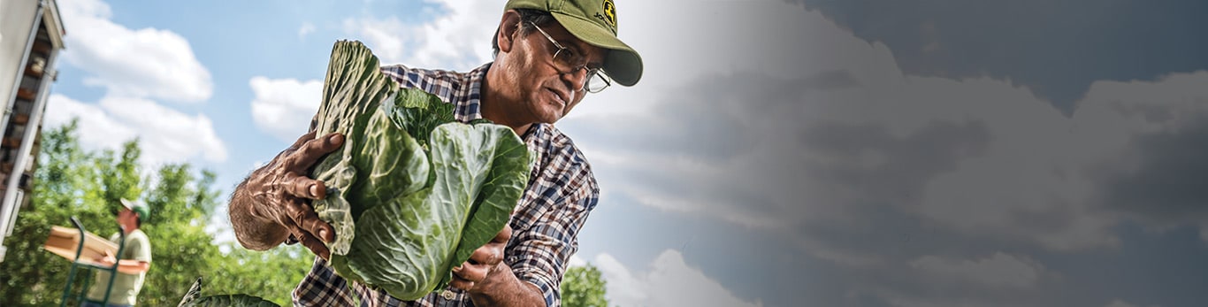 En man i skyddshjälm på en arbetsplats med utrustning från John Deere i närheten