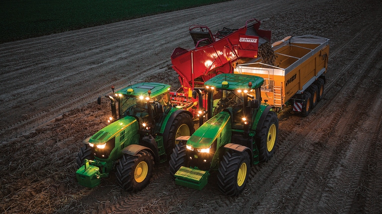 Traktorn som drar potatisexakthacken p&aring; natten t&ouml;mmer potatisen i en vagn som en annan traktor drar