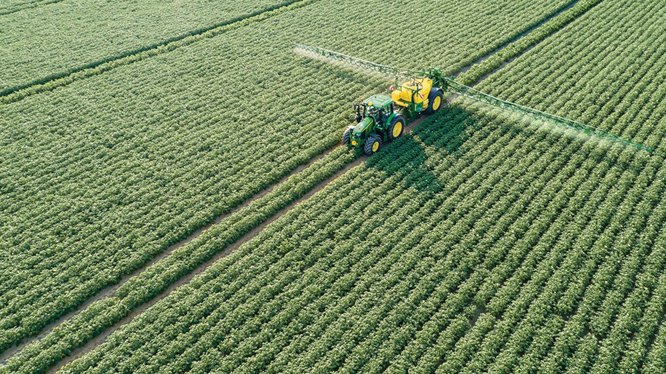 John Deere 6M-seriens traktor drar en M700 sl&auml;pande spruta i potatisf&auml;lt