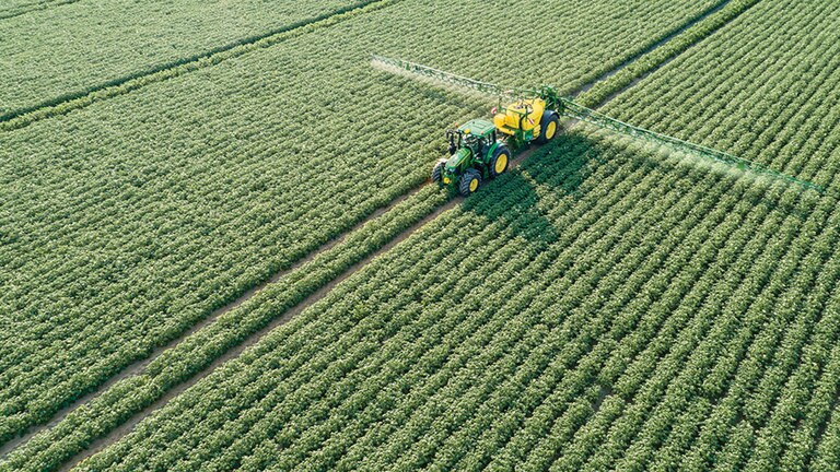 John Deere 6M-seriens traktor drar en M700 sl&auml;pande spruta i potatisf&auml;lt