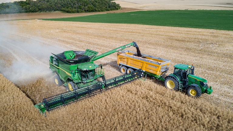 John Deere X-seriens sk&ouml;rdetr&ouml;skor t&ouml;mmer rapsfr&ouml; i spannm&aring;lsvagnar som dras av en John Deere-traktor