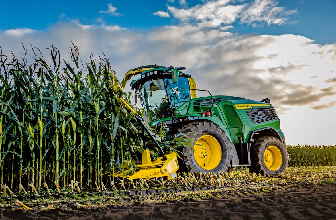 John Deere exakthack skördar majs på ett fält under blå himmel med moln.