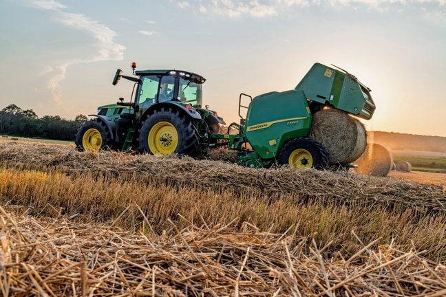 John Deere F442M-balpress dragen av en John Deere 6M-traktor som matar ut en halmbal