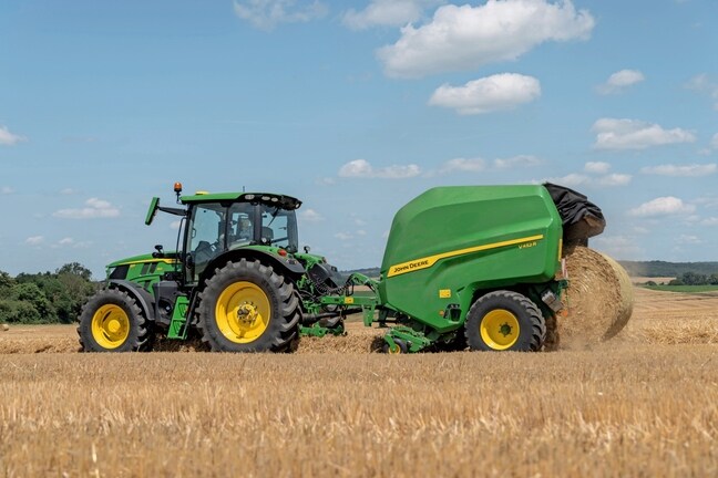 John Deere V452R på ett halmfält dragen av en John Deere 6R 150 som matar ut en bal
