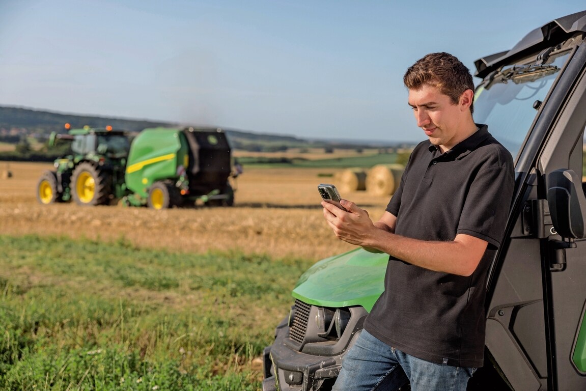 Person som kontrollerar baldokumentationsdata på mobiltelefonen med en John Deere VR-balpress i bakgrunden