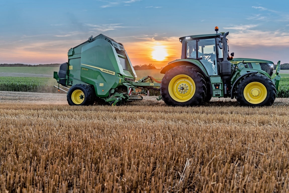 John Deere V462M på ett halmfält dragen av en John Deere 6M 150 under en solnedgång