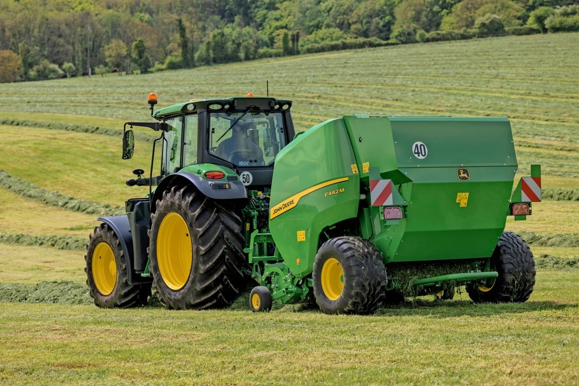 John Deere F442M-balpress dragen av en John Deere 6M-traktor på ett kuperat gräsfält