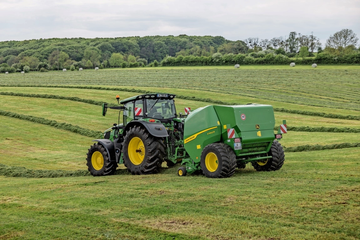John Deere F442R-balpress dragen av en John Deere 6M-traktor på ett kuperat gräsfält