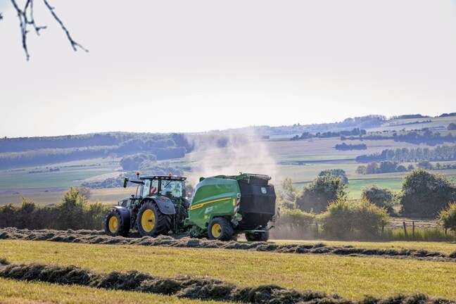 John Deere V462R dragen av en John Deere 6R 185-traktor som pressar hö